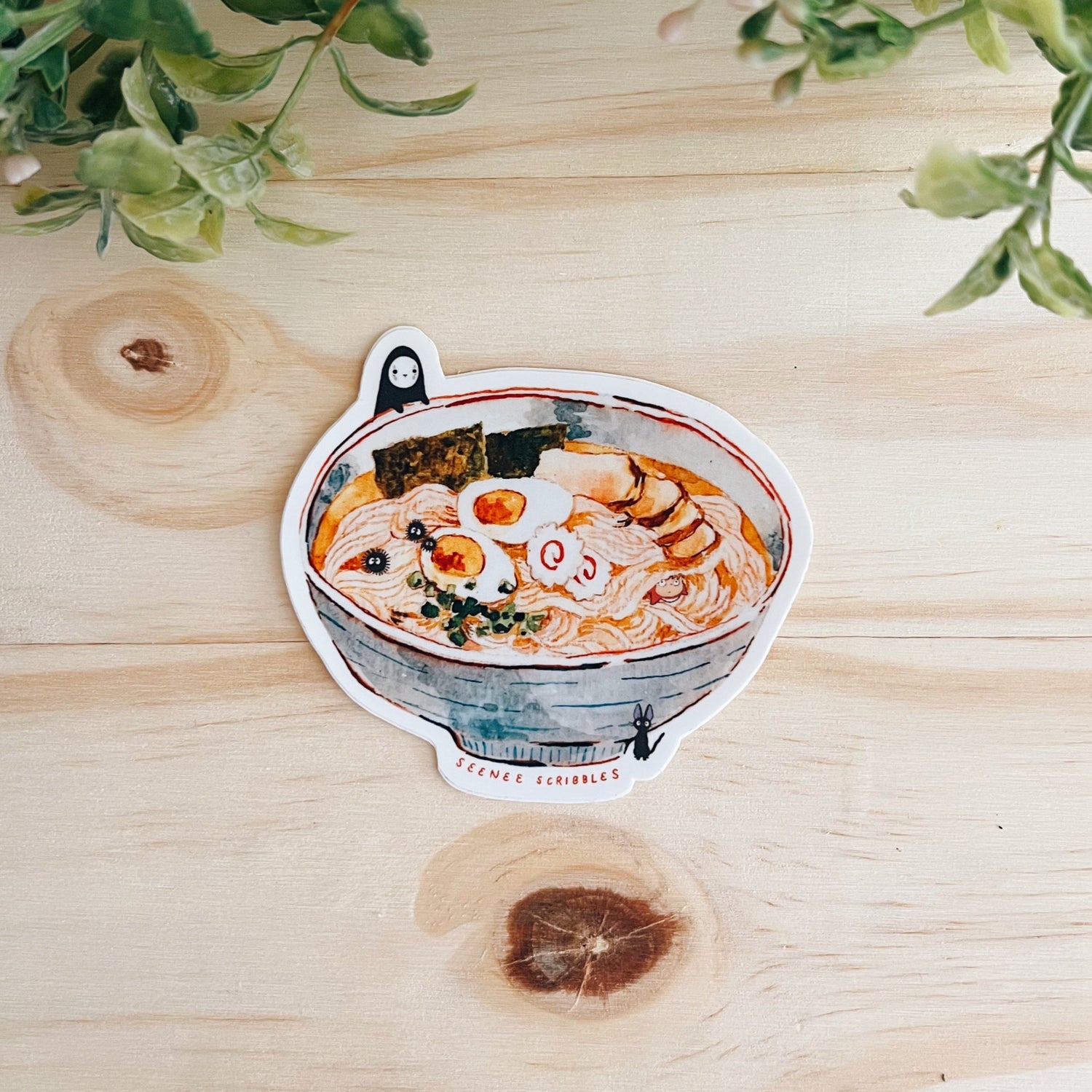 Watercolor painted sticker featuring various characters from Studio Ghibli films. The sticker is on a wooden desk with leaves at the top.